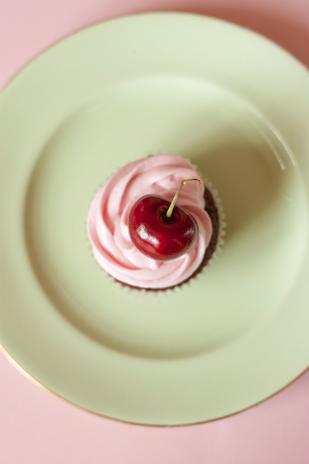 Pink frosted cupcake with a cherry, seen from above